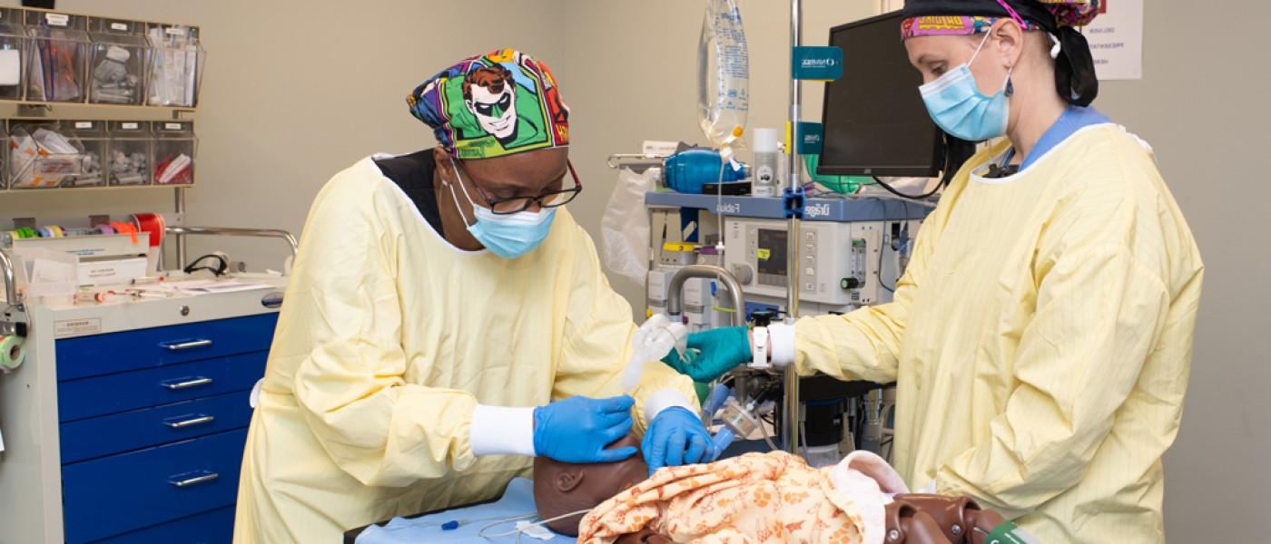 一名英国东北大学卫生专业的学生穿着手术服在病人模拟器上工作