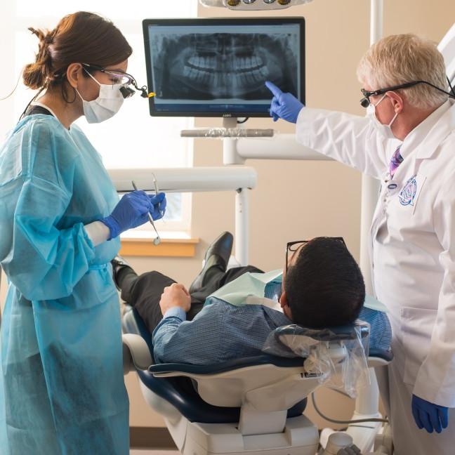 一名学生和教师在正规澳门赌场网络口腔健康中心检查病人的牙科x光片